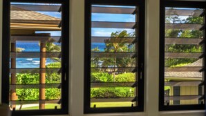 Trois fenêtres équipées de stores horizontaux, chacune offrant une vue sur un paysage tropical, avec une végétation luxuriante et une étendue d’eau.