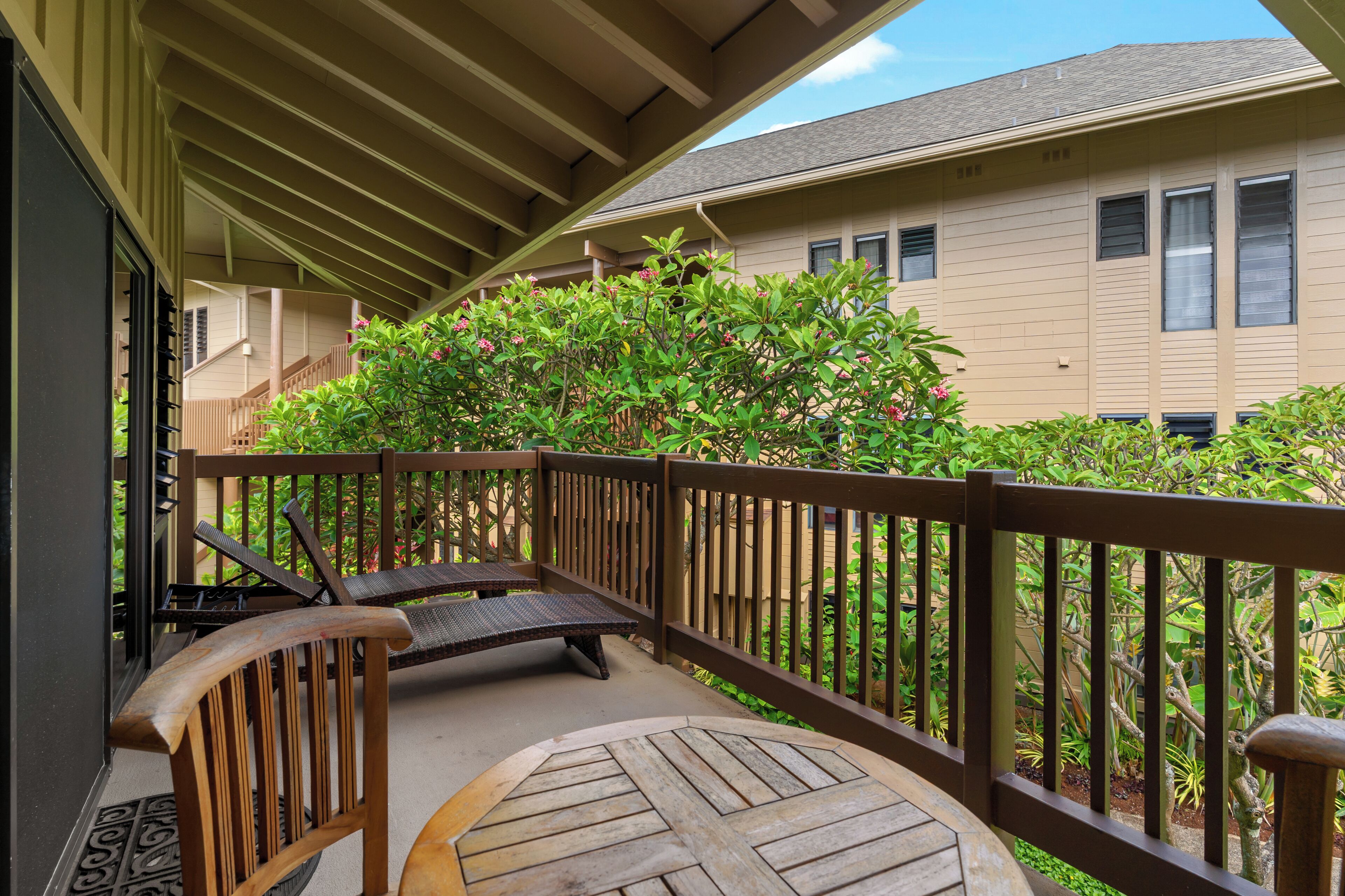 A covered outdoor area with a wooden deck, a round table, and two lounge chairs.