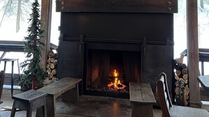 A stone fireplace with a fire, wooden benches, and a Christmas tree in a covered outdoor area.