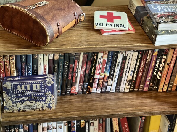 Una estantería con una variedad de libros, DVD y un botiquín de primeros auxilios de 'Ski Patrol'.