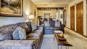 Ein Wohnzimmer mit einem großen Gemälde, einer Sofagarnitur, einem Couchtisch und einem Essbereich im Hintergrund.