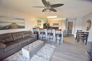 A modern living room with a leather sofa, a white ottoman, and a bar area with stools.