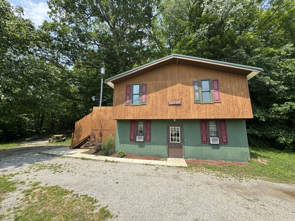 A two-story wooden house with a green exterior and red shutters, labeled "SANDY RUNG."