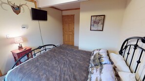 A bedroom with a bed, a TV mounted on the wall, a wooden door, and a framed picture.
