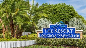 En skylt för The Resort Longboat Key Club, med en vacker trädgård och palmer.