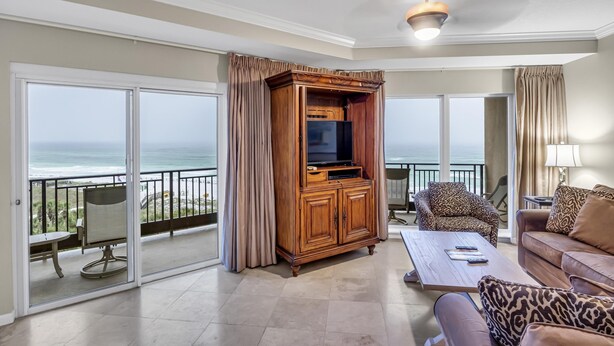 Ein geräumiges Wohnzimmer mit einer großen Holzunterhaltungsecke, einer Couch und einem Couchtisch. Ein Balkon bietet Blick aufs Meer.