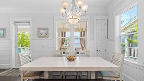 Une salle à manger avec une grande table, des murs blancs et un lustre.