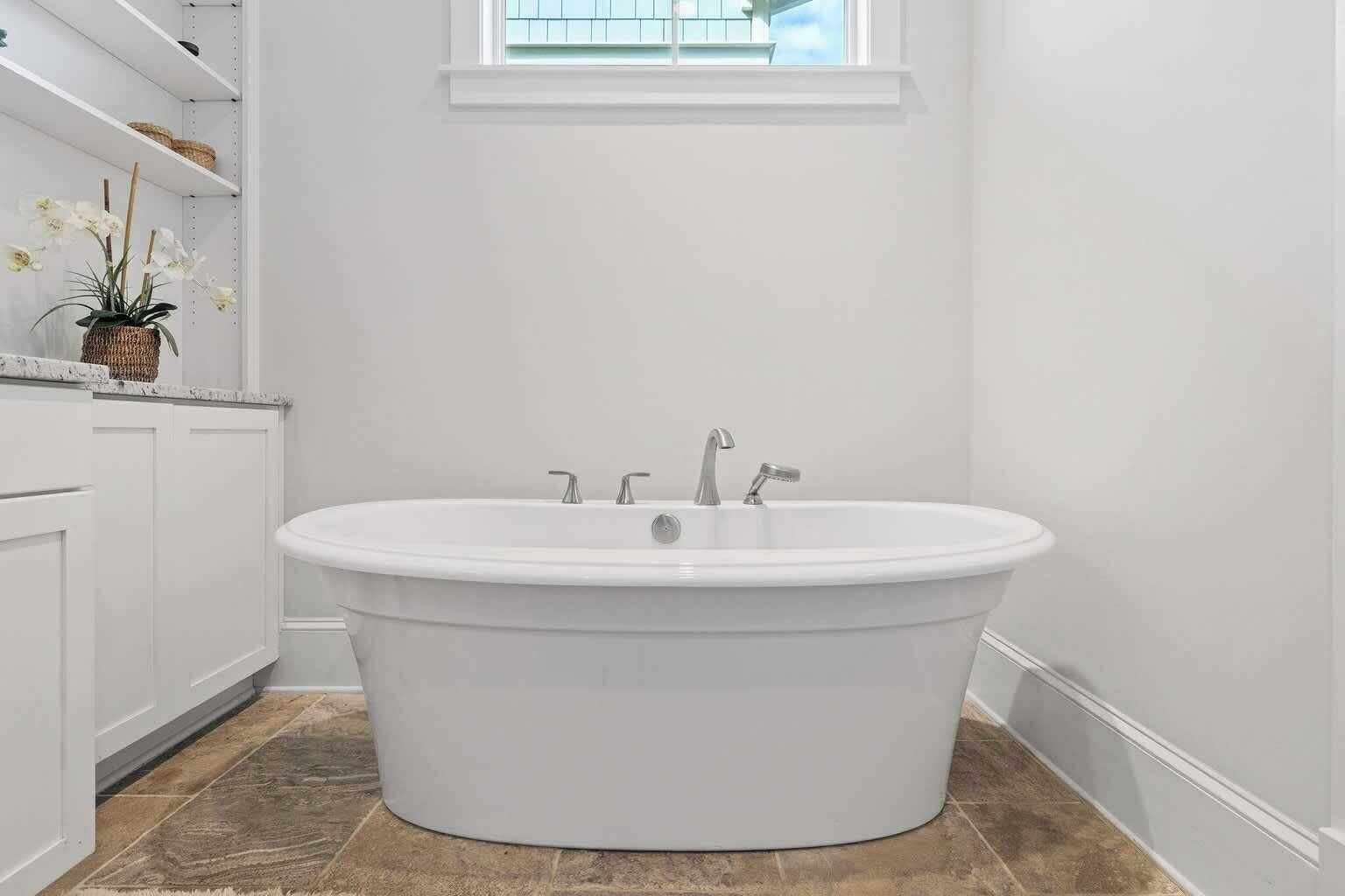 A white freestanding bathtub in a bathroom with a window above it.