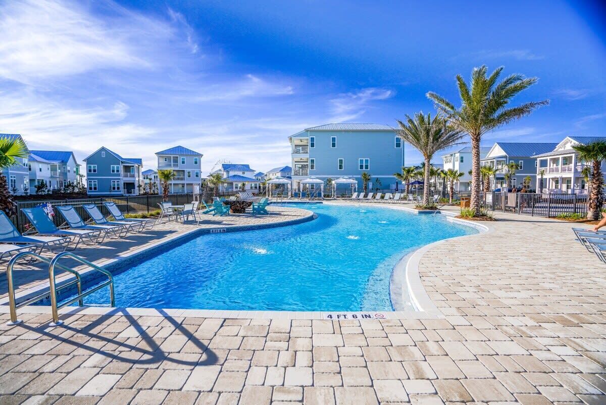 Una piscina con sillas de descanso y palmeras, rodeada de edificios de varios pisos.