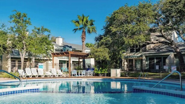 A swimming pool with lounge chairs, a pergola, and a building with a balcony.