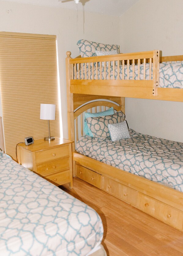 A bunk bed with a wooden frame, a bedside table with a lamp, and a patterned bedspread.