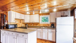 A kitchen with wooden cabinets, a microwave, a refrigerator, and a window with a view of trees.