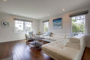 Un salon spacieux avec un grand canapé d’angle blanc, une table basse et un tableau accroché au mur.