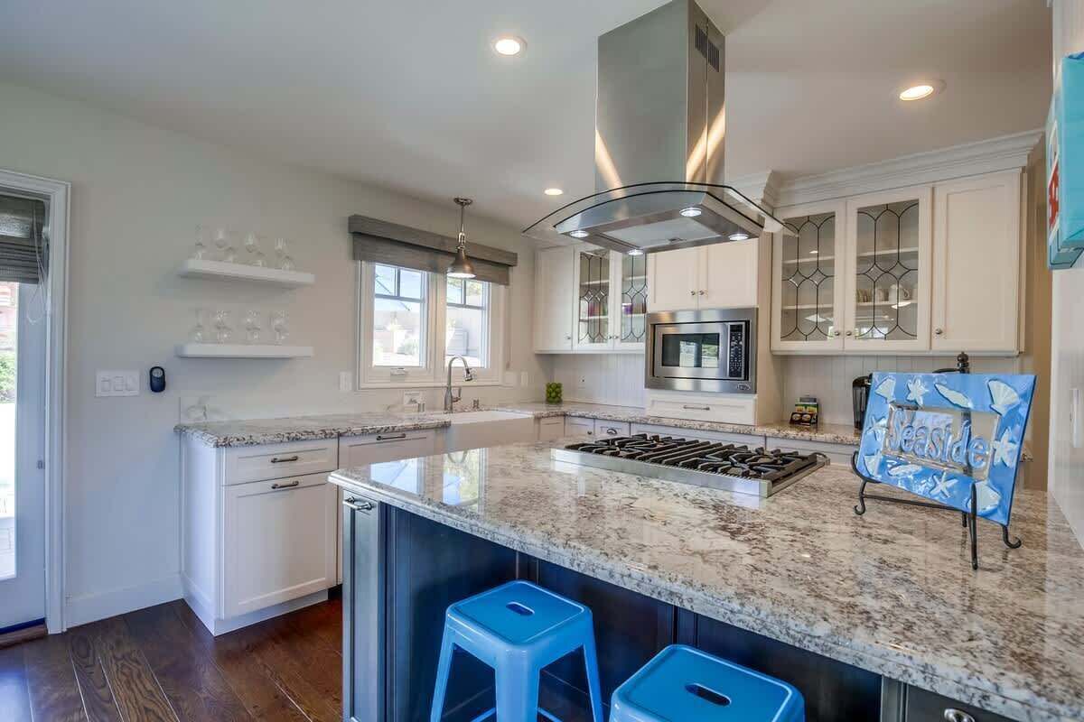A modern kitchen with white cabinetry, a central island, a stainless steel range hood, and a blue sign with 'Beside' on it.