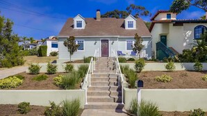 A two-story house with a front porch, a staircase leading to the front door, and a well-maintained garden with various plants. - Village Life, walk to the village of La Jolla (La Jolla)