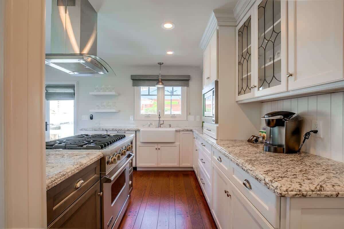 Una cocina con gabinetes blancos, encimera de granito, campana extractora de acero inoxidable y una ventana sobre el fregadero.