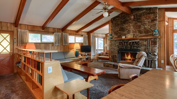 A cozy living room with a stone fireplace, wooden beams, a ceiling fan, and a television. - (99) Yosemite Mountain Lodge at The Redwoods In Yosemite (Wawona)