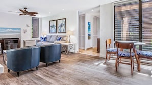 A modern living room with a sofa, two ottomans, a TV, and a dining area with chairs. - Totally renovated, closest to the beach! (Kihei)