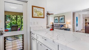 A modern kitchen with a marble countertop, a ceiling fan, and a framed map on the wall. - Totally renovated, closest to the beach! (Kihei)