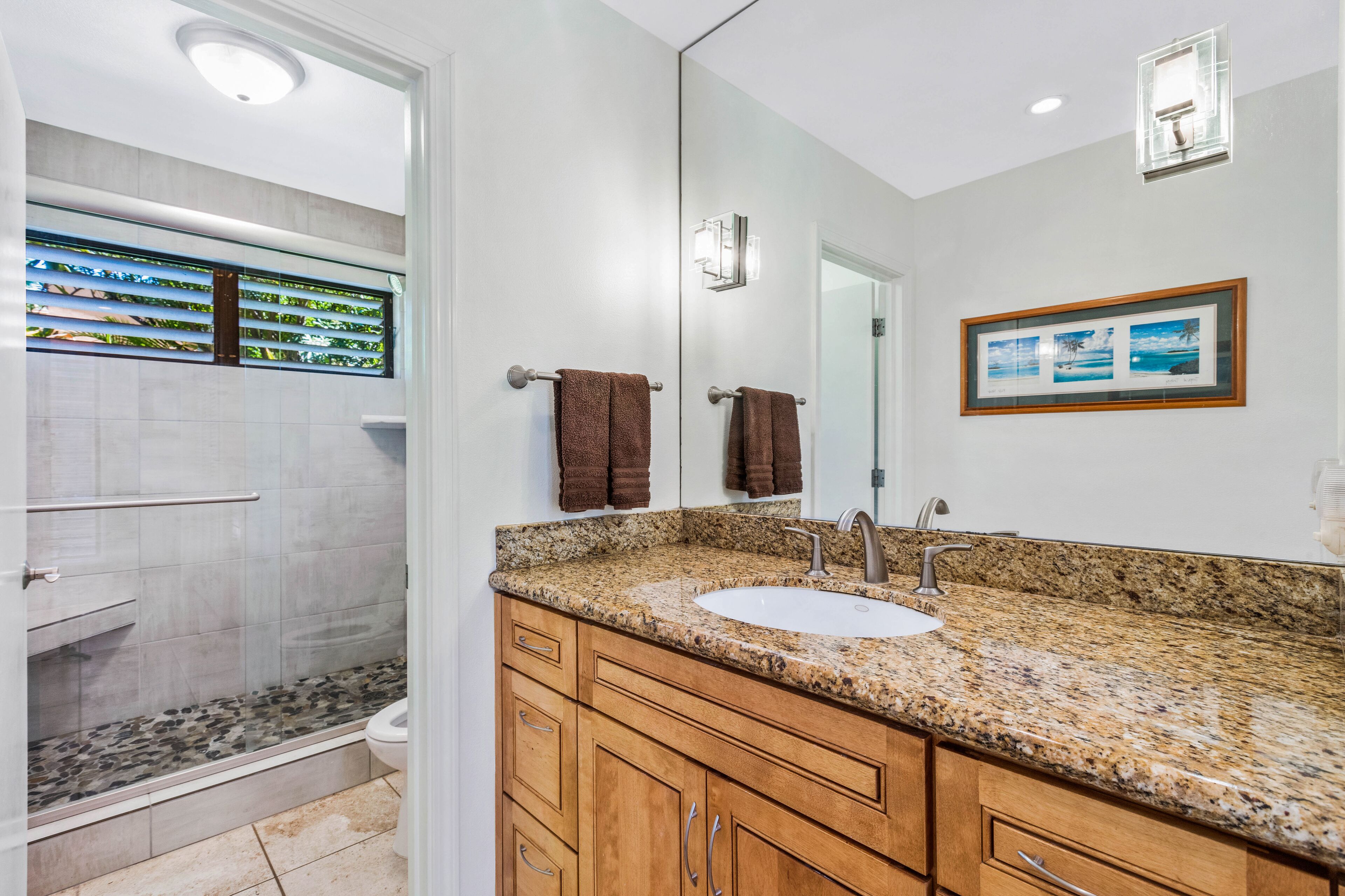 A bathroom with a granite countertop, a sink, a mirror, and a shower area.