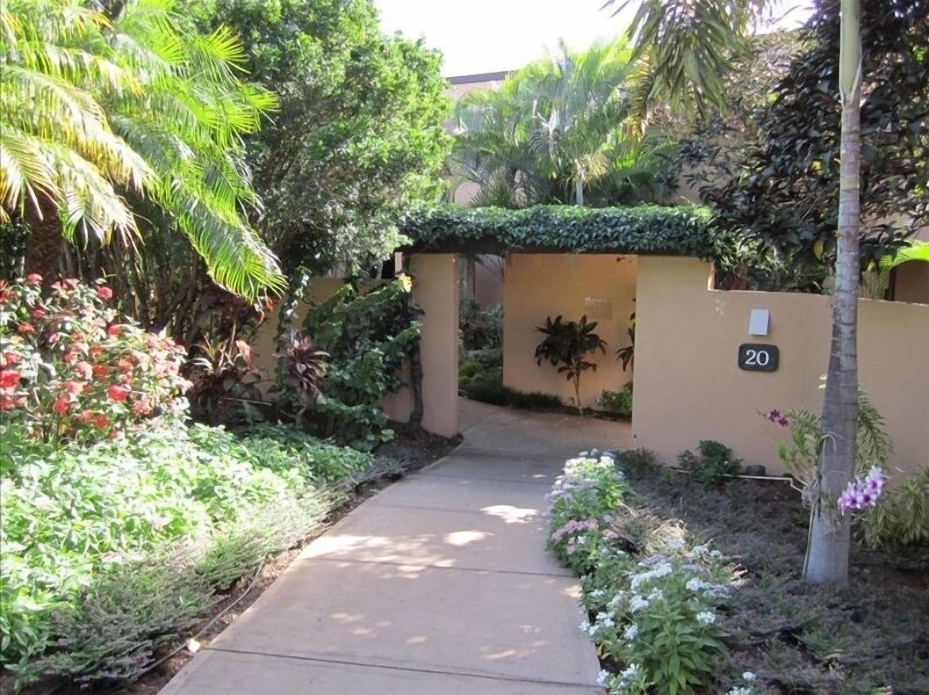 A pathway leading to a building with a number '20' sign, surrounded by lush greenery and various plants.