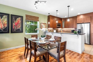 Una cocina moderna con armarios de madera, una isla central y un comedor con mesa y sillas de vidrio.