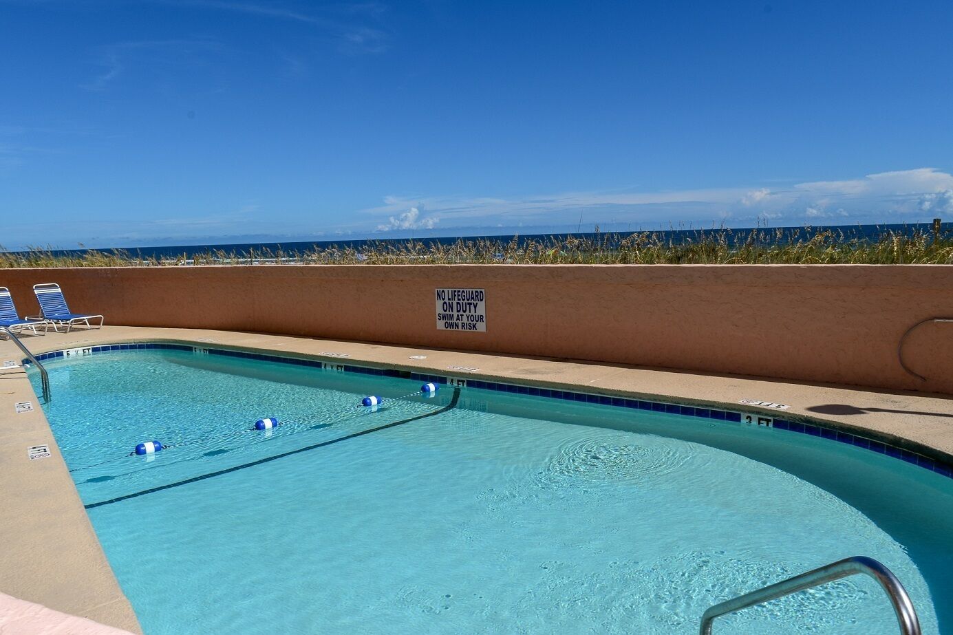 Una piscina con un cartel de socorrista, sillas de descanso y vistas a la playa.