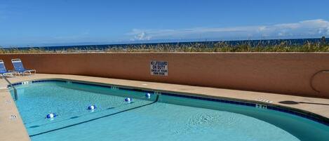 Una piscina con un cartel de socorrista, sillas de descanso y vistas a la playa.