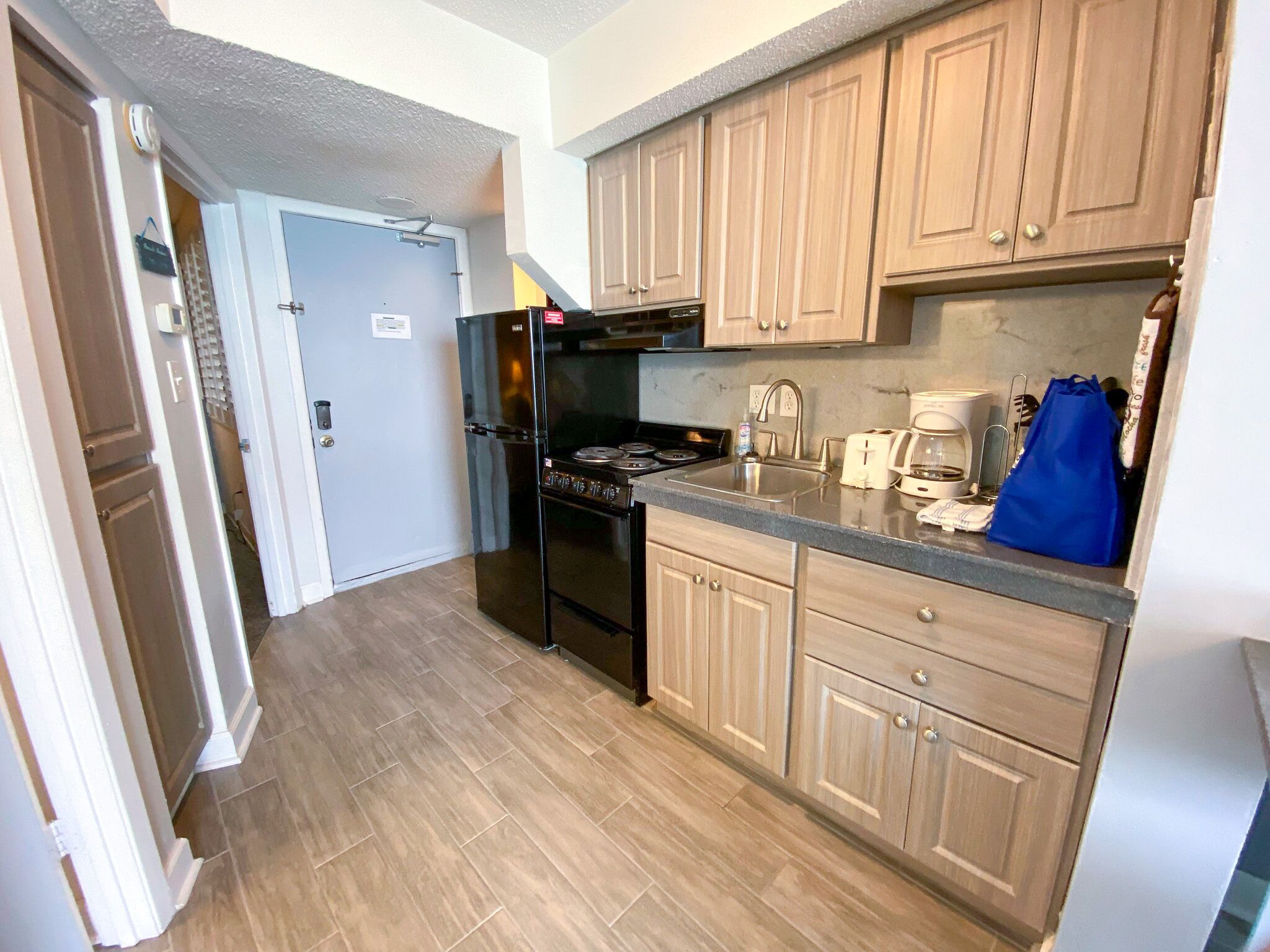 A compact kitchen with wooden cabinets, a black refrigerator, a stove, and a sink.