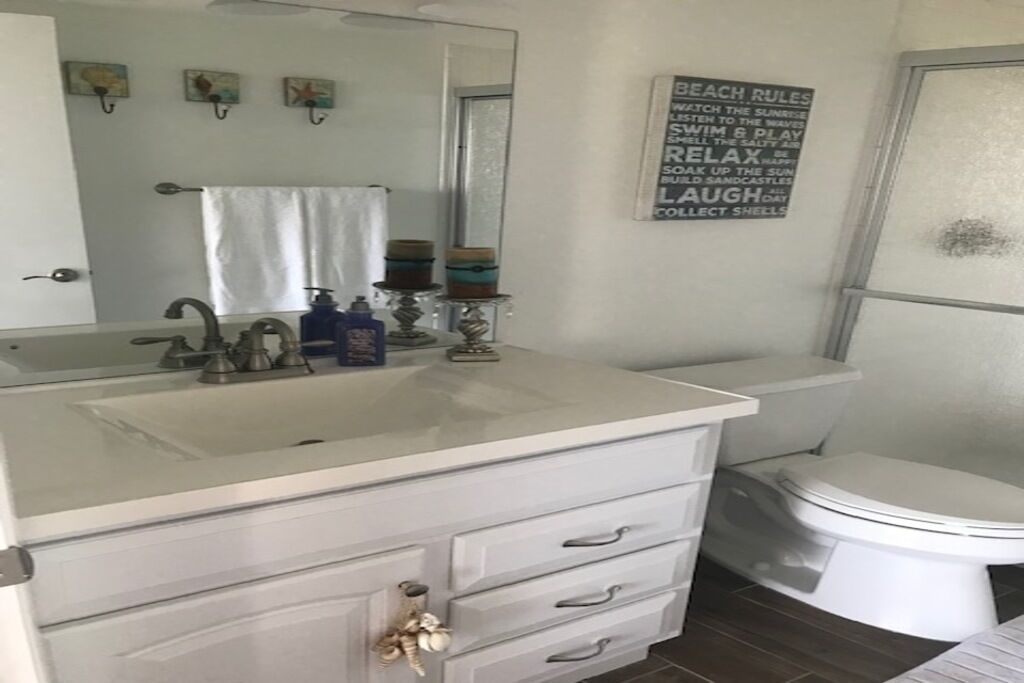 A bathroom with a white sink, vanity, and toilet. There is a towel hanging on the wall and a sign with beach rules.
