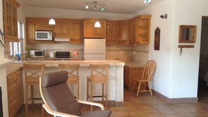 Une cuisine avec des meubles de rangement en bois, un four à micro-ondes, une cuisinière et un réfrigérateur. On y trouve deux tabourets de bar et une chaise.