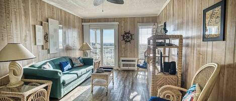 A living room with a ceiling fan, a green sofa, wicker furniture, and a view through a glass door.