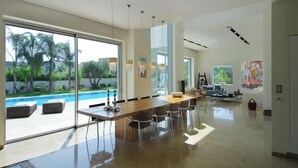 A spacious modern dining area with a long table and chairs, large windows, and a view of a swimming pool. - Luxurious villa with fenced swimming pool in the Caesarea Golf area  (Caesarea)