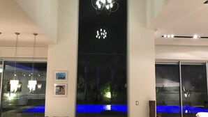 A modern dining area with a large wooden table and chairs, a chandelier, and a view of a blue-lit water feature through a glass wall. - Luxurious villa with fenced swimming pool in the Caesarea Golf area  (Caesarea)