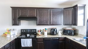 A kitchen with dark wood cabinets, a stove, a microwave, and a coffee maker. - “Ca C’est Bon” (Lake Charles)
