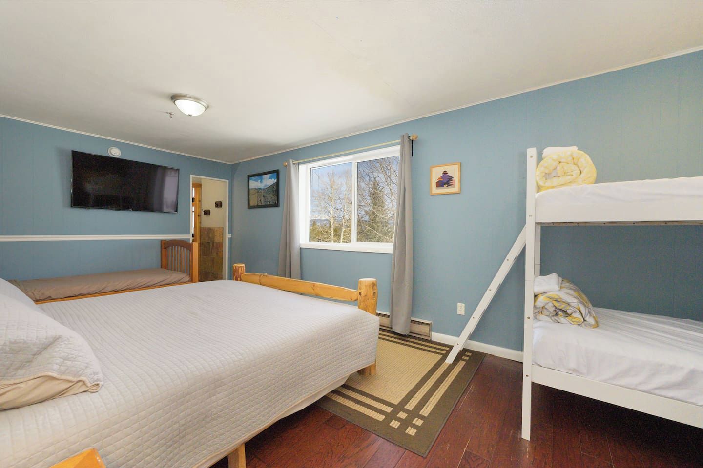 A room with a bed, a bunk bed, a television, a window with curtains, and a door.