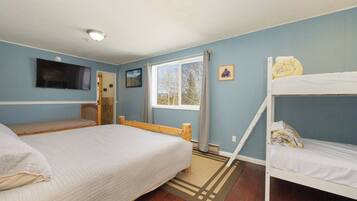 A room with a bed, a bunk bed, a television, a window with curtains, and a door.