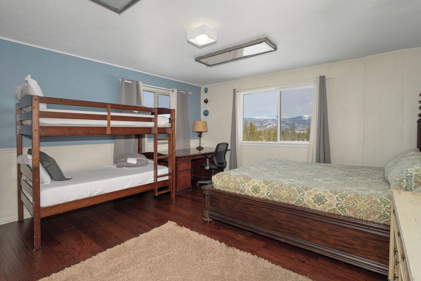 Ein Schlafzimmer mit Etagenbett, Schreibtisch mit Stuhl, Fenster mit Blick und Bett mit gemustertem Überwurf.