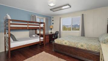 Ein Schlafzimmer mit Etagenbett, Schreibtisch mit Stuhl, Fenster mit Blick und Bett mit gemustertem Überwurf.