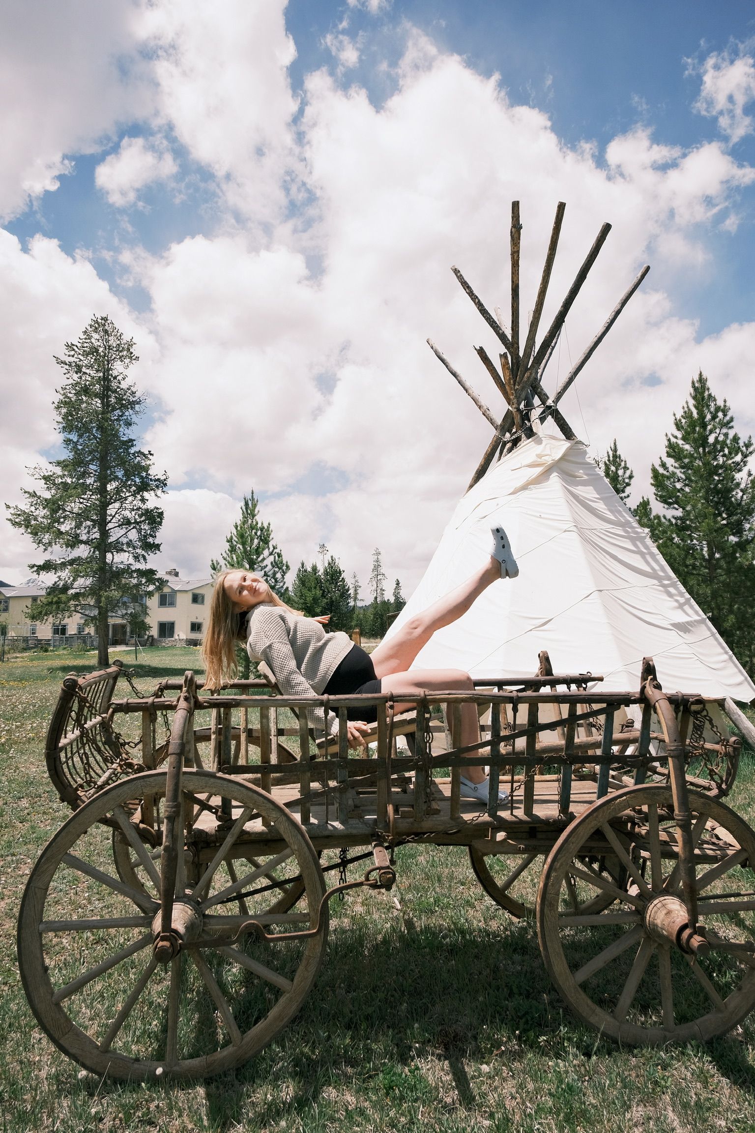 A person lying on a wagon with a teepee structure behind them.