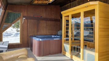 A wooden cabin with a hot tub, a sauna, and a view of a snowy landscape.