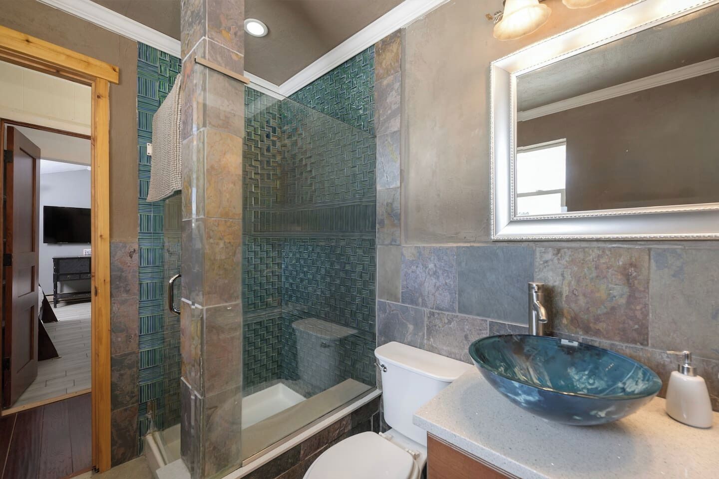A bathroom with a glass-enclosed shower, a glass bowl sink, and a toilet.
