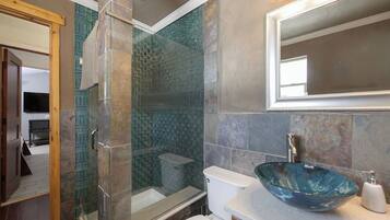 A bathroom with a glass-enclosed shower, a glass bowl sink, and a toilet.