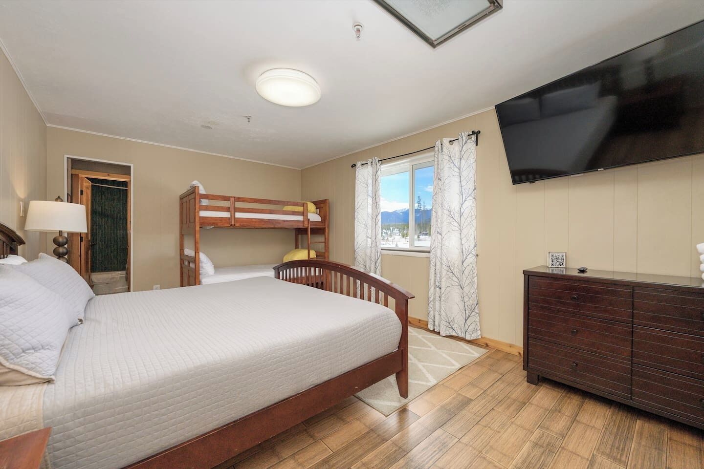 A bedroom with a bunk bed, a single bed, a dresser, a television, and a window with curtains.