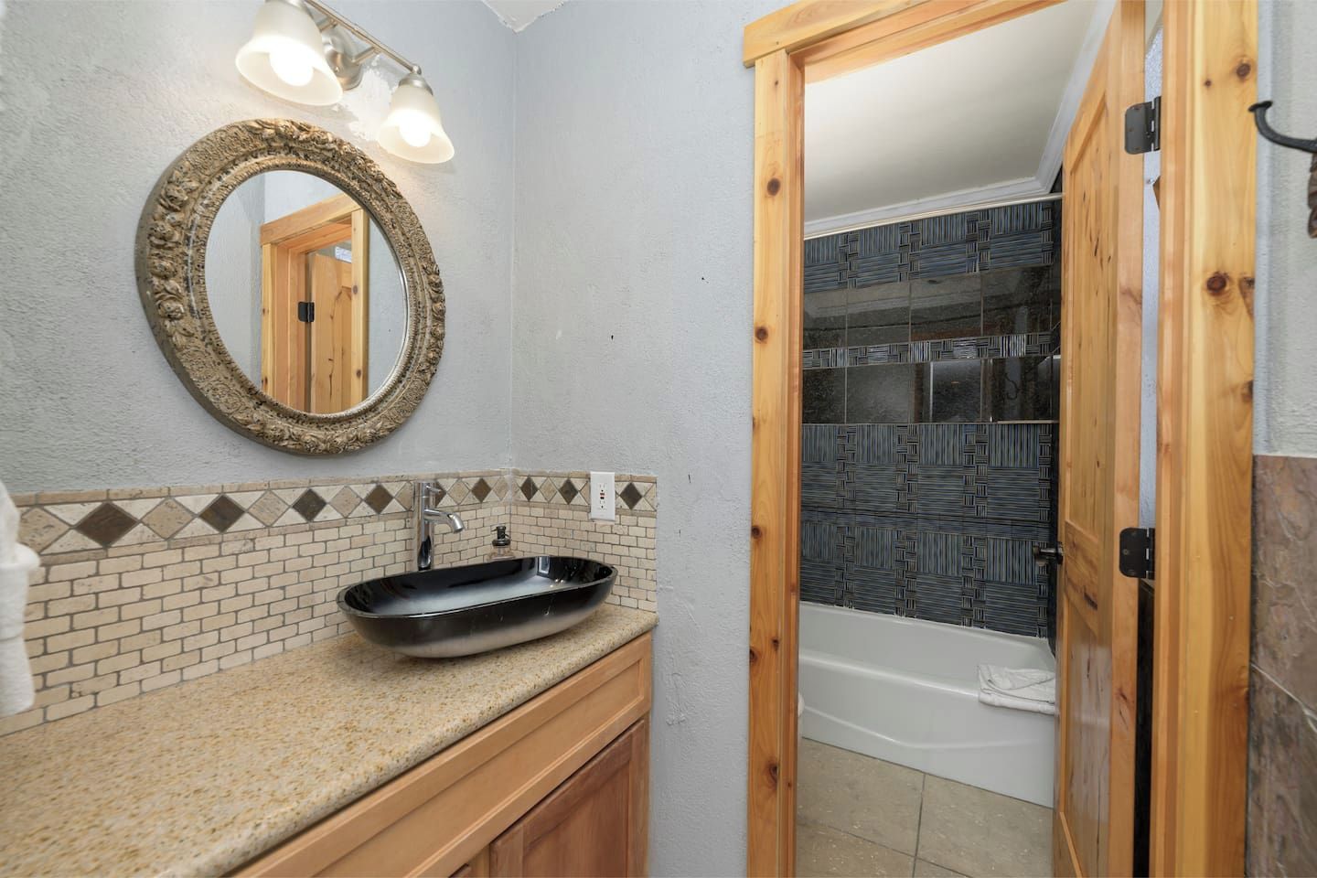 A bathroom with a freestanding sink, a mirror with a decorative frame, and a shower area with patterned tiles.