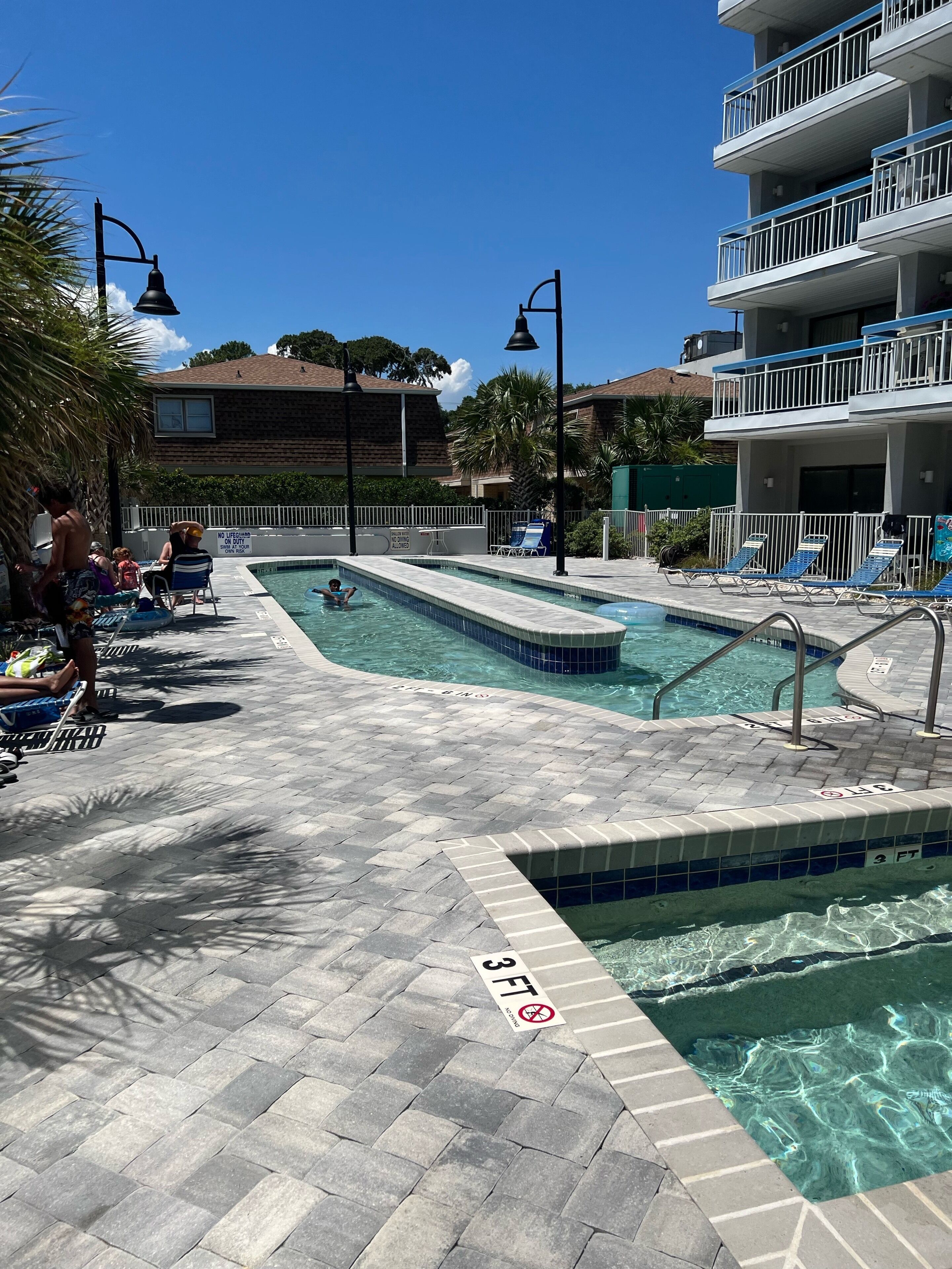 A pool area with clear water, lounge chairs, and a lifeguard stand.