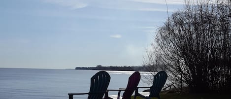 Three Adirondack chairs facing a lake with a clear sky.