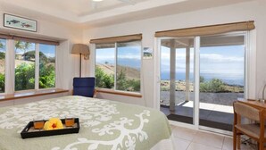 A bedroom with a bed, a desk, and a chair. There are two windows with curtains, and a view of the outdoors. - Hale Kohola ~ Spacious, Super Views - 30 Day Minim (Waimea)