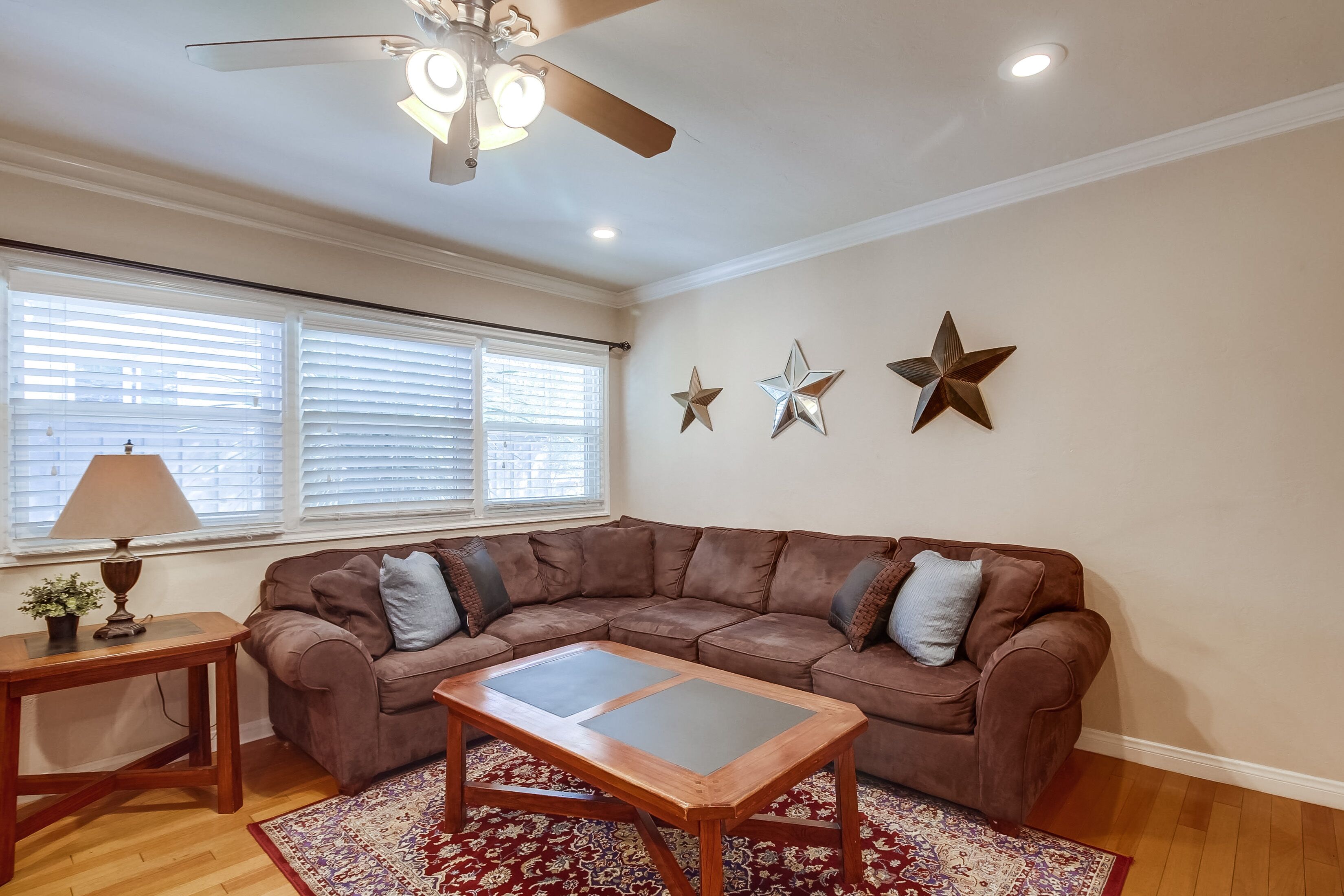 A living room with a brown sectional sofa, a wooden coffee table, a patterned rug, a lamp, and decorative star-shaped wall art.