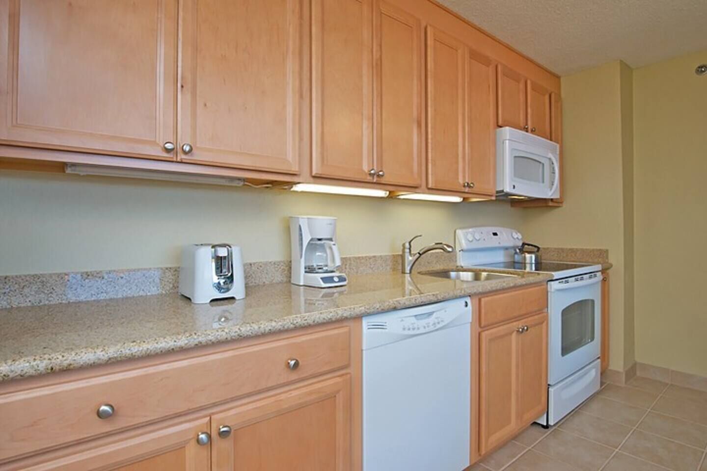 A kitchen with wooden cabinets, a microwave, a coffee maker, a dishwasher, and an oven.